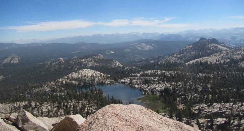 From a high point of view, an alpine lake rests amongst trees, rocks and mountains.